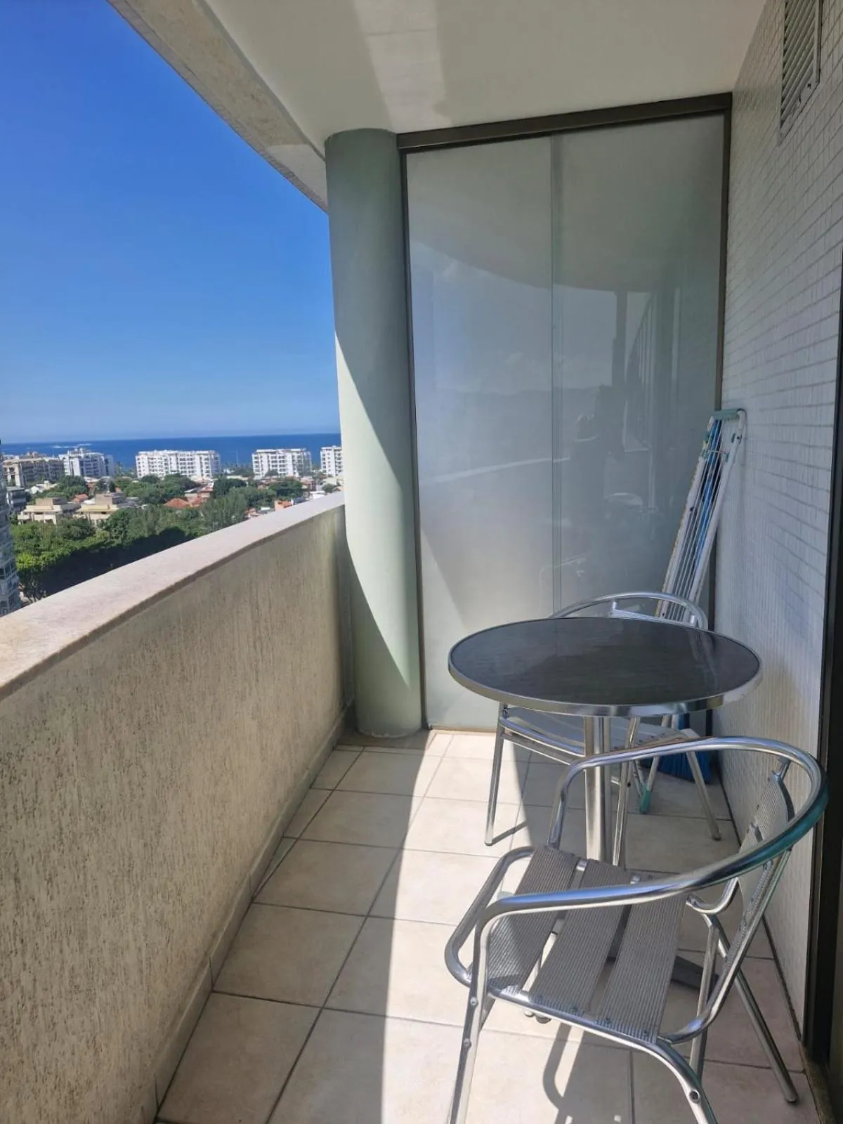 Un balcon avec une table et des chaises offre une vue sur la mer et la ville.