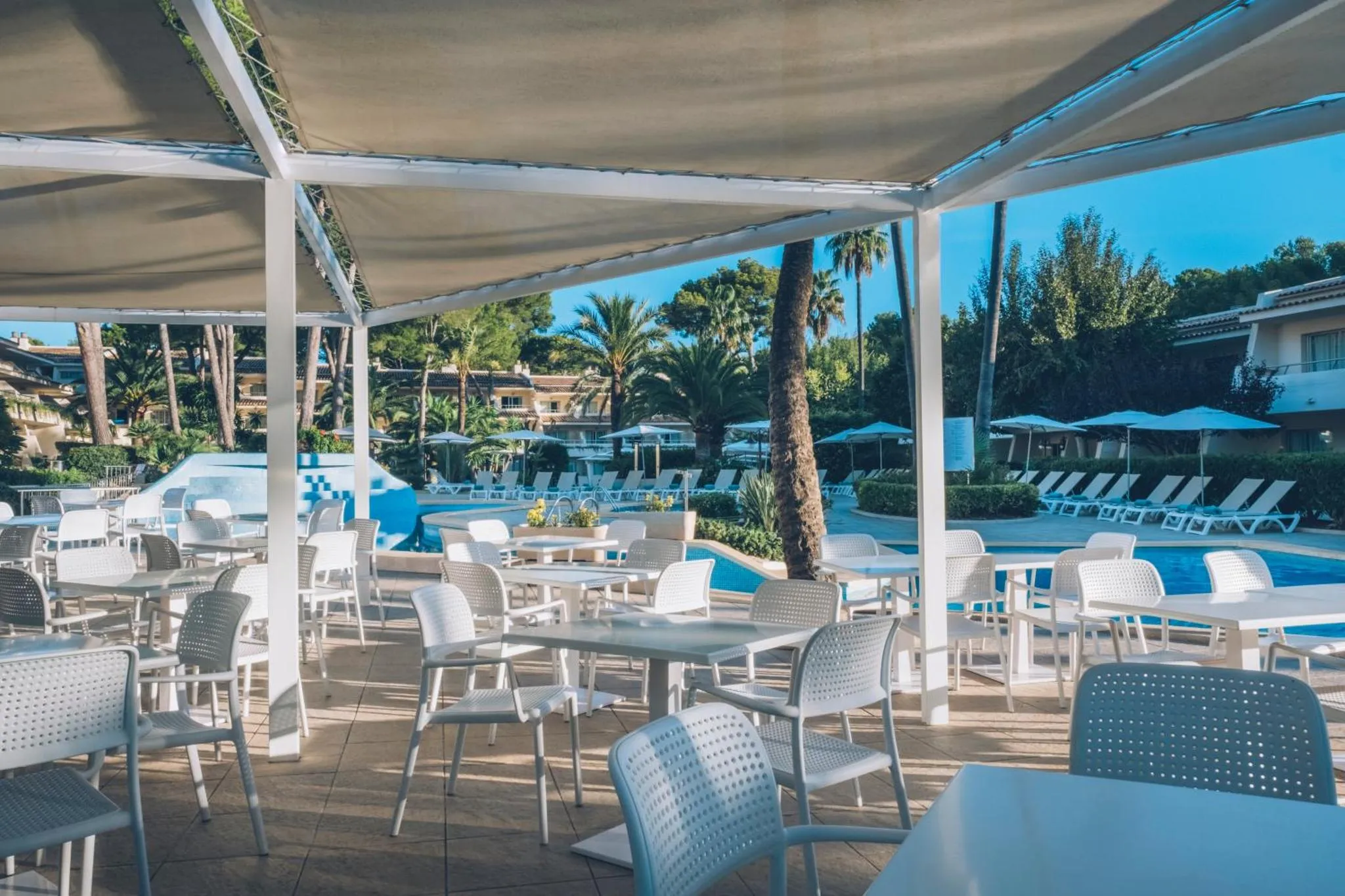 Terrasse ombragée avec tables et chaises près d'une piscine.