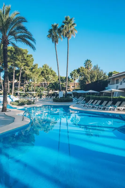 Une piscine turquoise reflète le ciel bleu sous les palmiers.