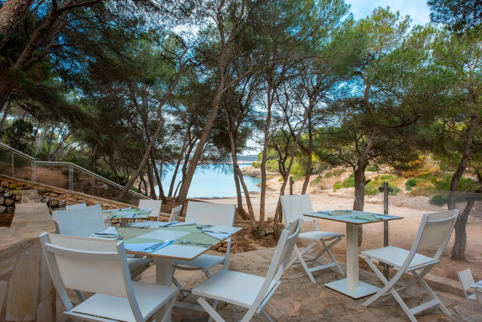 Tables et chaises blanches disposées sur une terrasse en gravier, face à la mer.
