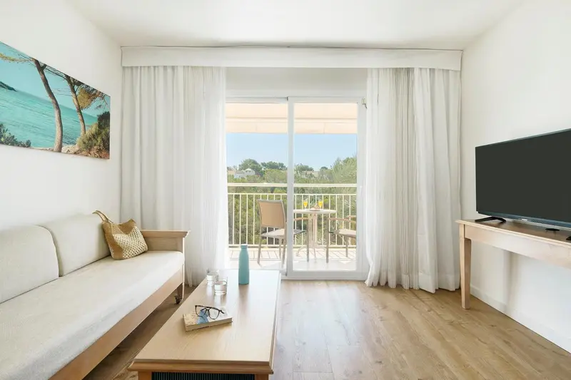 Un salon clair s'ouvre sur un balcon avec vue sur la vegetation.