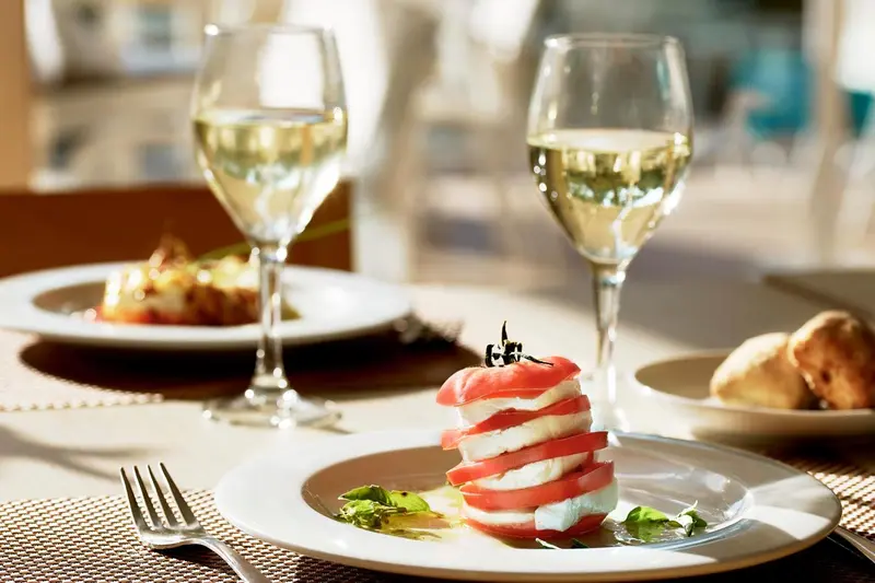 Deux verres de vin blanc et une assiette de salade caprese sont servis sur une table.