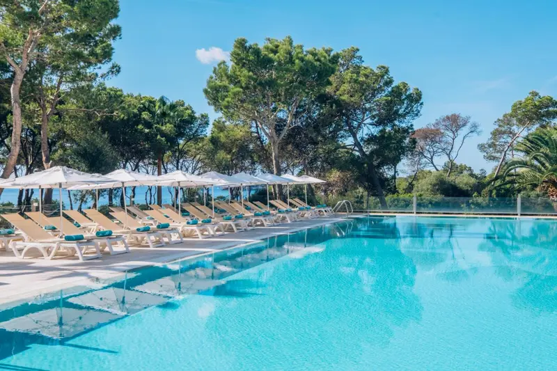 Transats alignés au bord d'une piscine turquoise sous des parasols blancs.