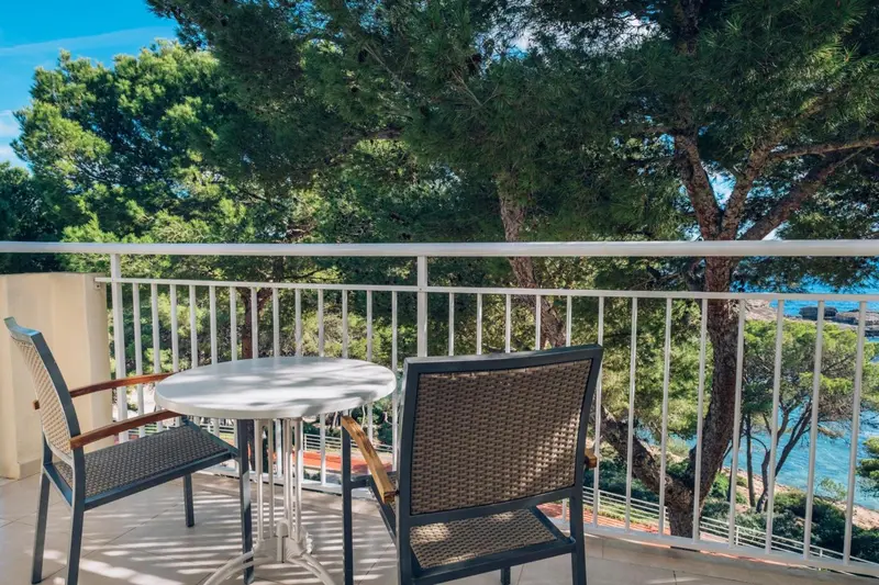 Une terrasse avec une table et des chaises offre une vue sur la mer et la végétation.