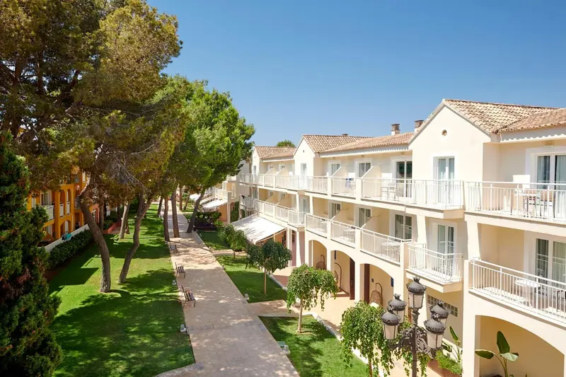 Vue d'un ensemble de bâtiments blancs avec des balcons et des terrasses, entourés d'une végétation luxuriante.
