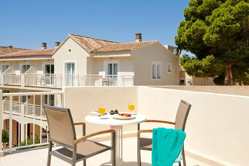 Deux fauteuils et une table basse avec des boissons sur une terrasse ensoleillée.