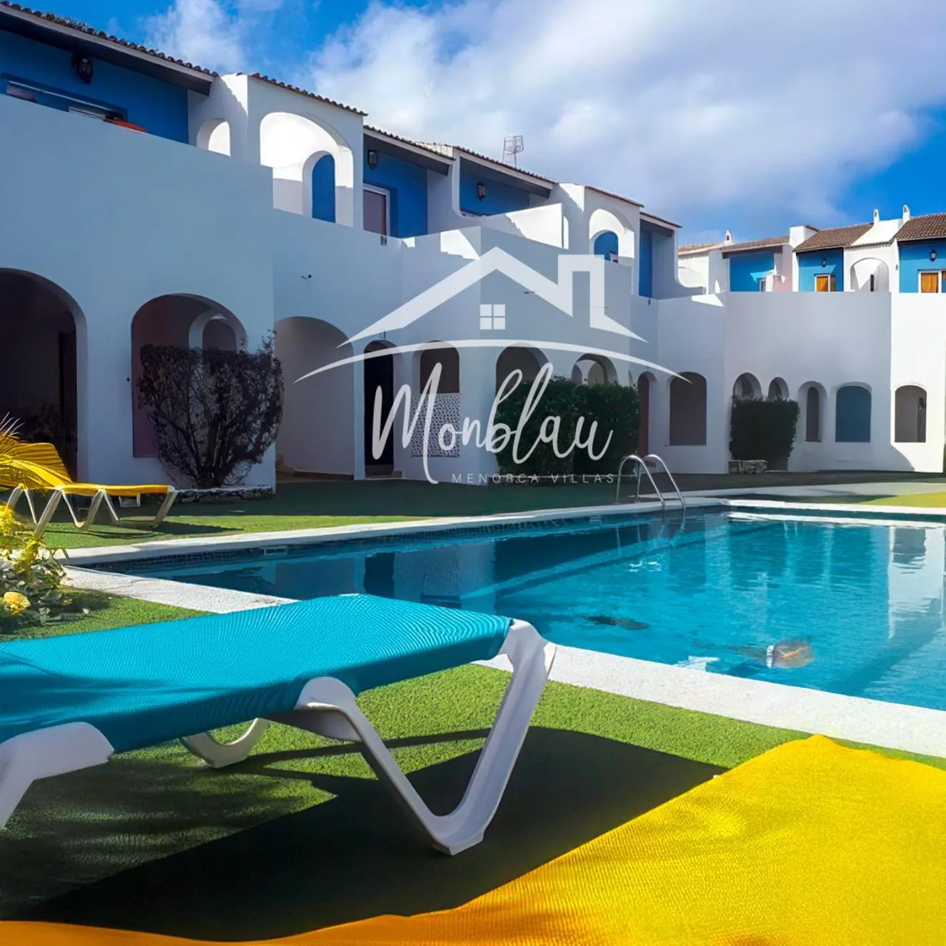 Transats bleus au bord d'une piscine turquoise devant un bâtiment blanc.