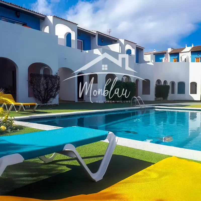 Transats bleus au bord d'une piscine turquoise devant un bâtiment blanc.