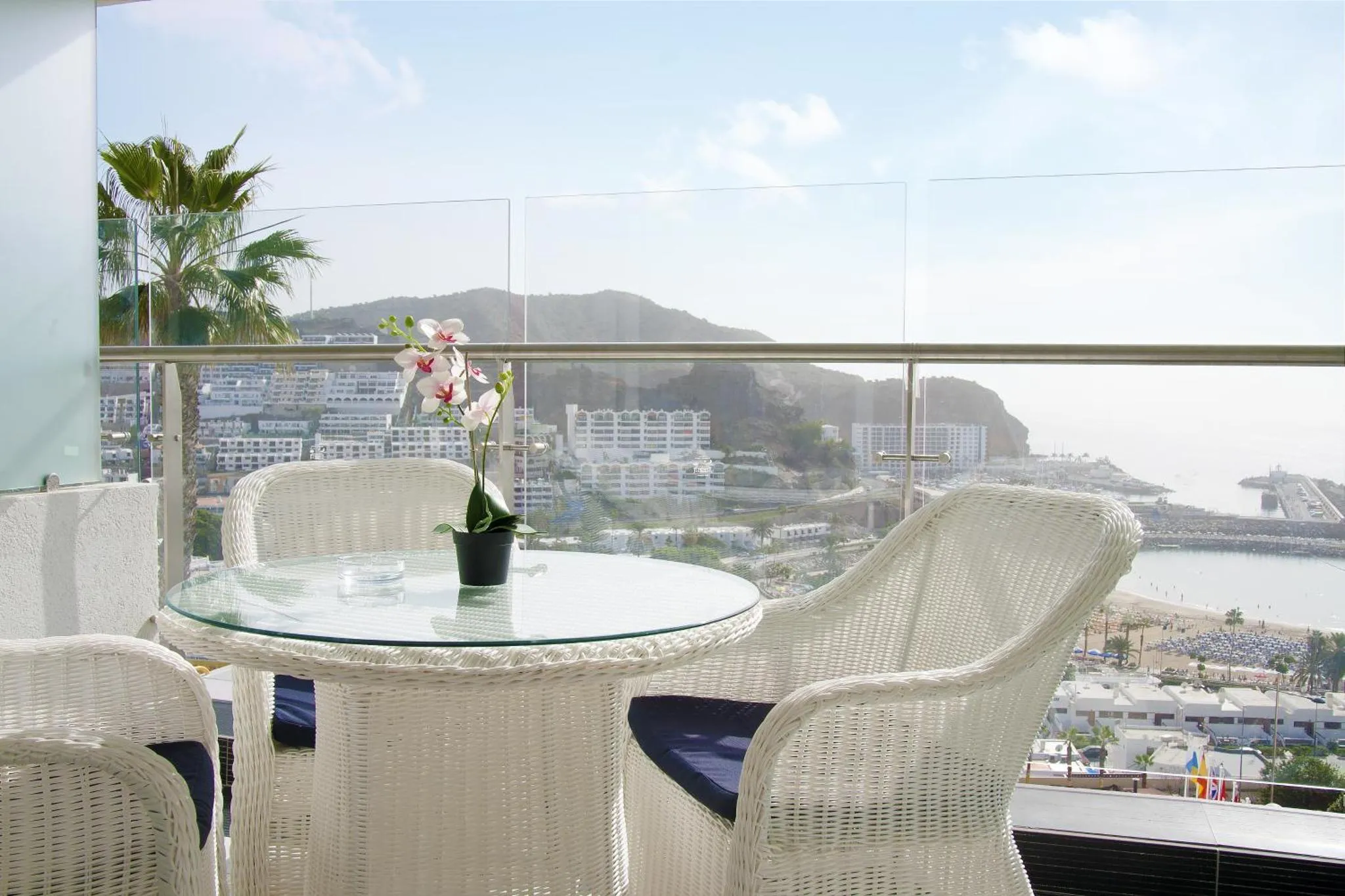 Terrasse avec mobilier blanc offrant une vue sur la mer et les montagnes.