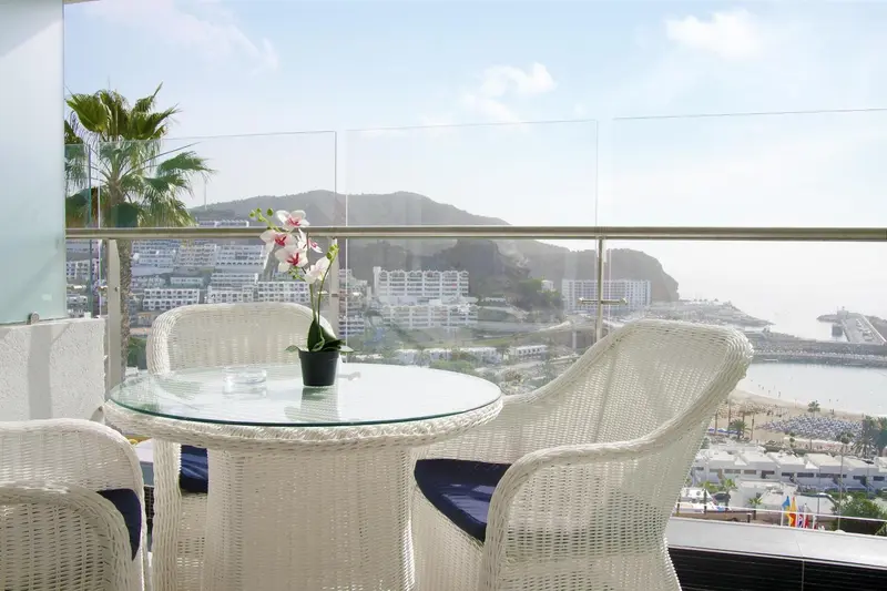 Terrasse avec mobilier blanc offrant une vue sur la mer et les montagnes.