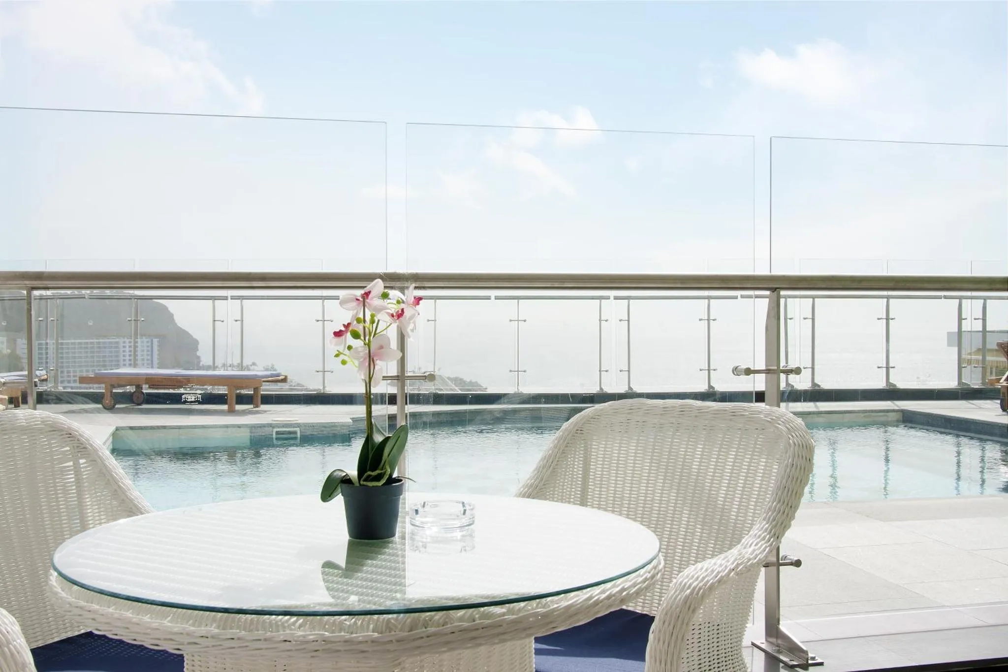Terrasse avec mobilier blanc et piscine au premier plan, vue sur la mer.