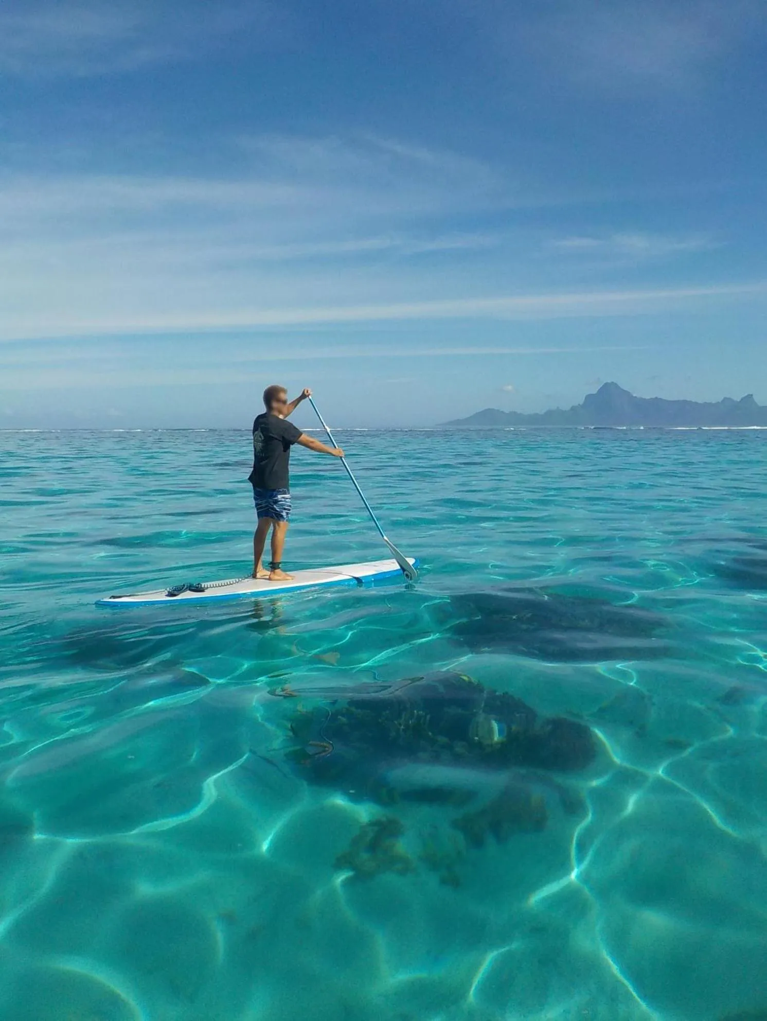 Une personne se tient debout sur une planche de paddle au milieu d'une eau turquoise et claire.