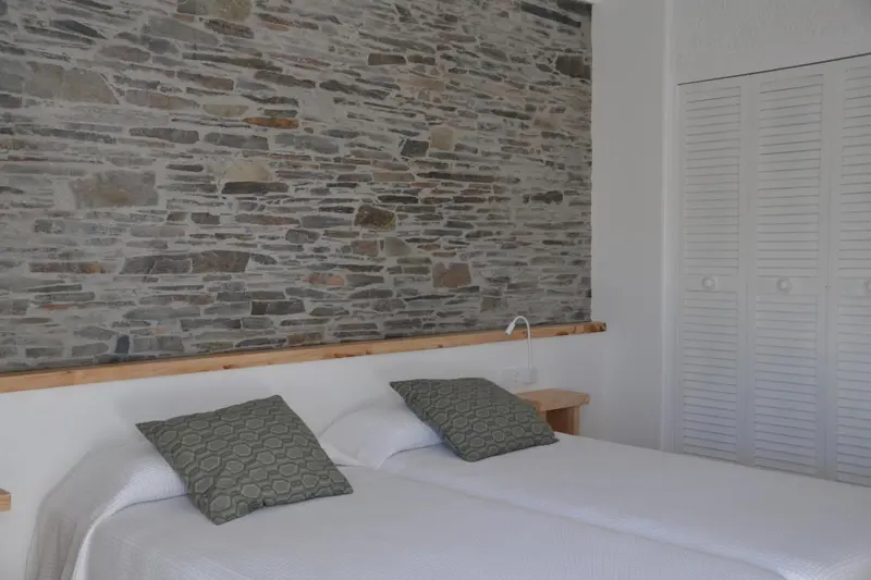Une chambre lumineuse avec un mur en pierres apparentes et un lit recouvert de linge blanc.