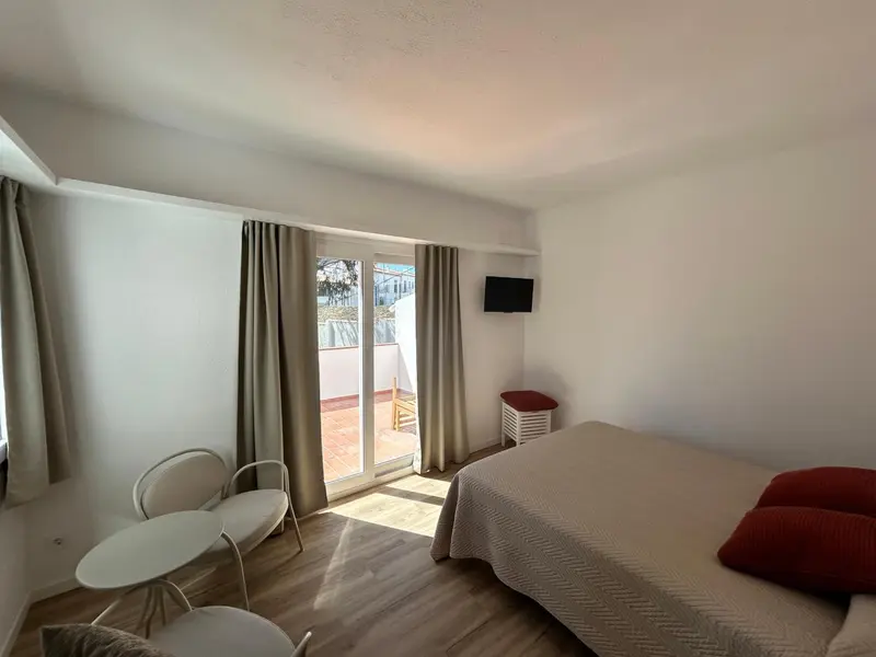 Une chambre lumineuse avec un lit et un coin salon donnant sur une terrasse.