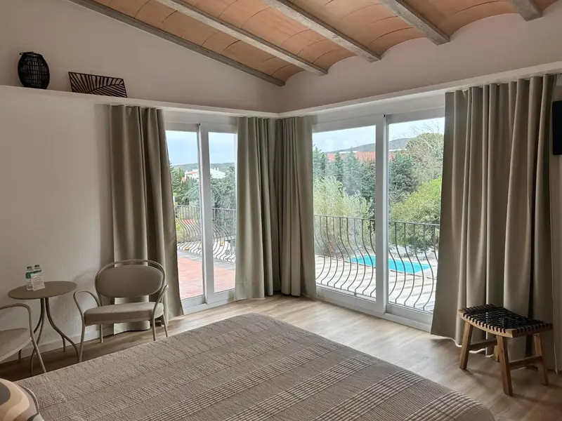 Une chambre lumineuse s'ouvre sur une vue dégagée et une piscine.