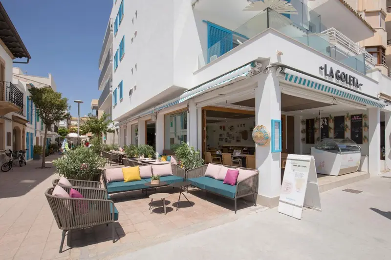 Terrasse ombragée avec mobilier d'extérieur et façade d'un bâtiment blanc.