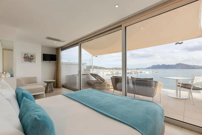 Une chambre lumineuse s'ouvre sur une terrasse avec vue sur la mer et un port de plaisance.