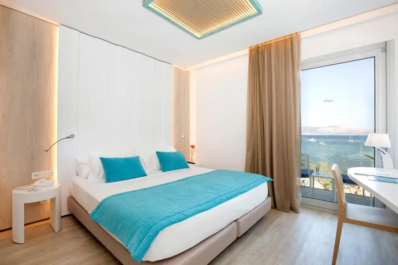 Une chambre lumineuse avec un lit turquoise et une vue sur la mer.