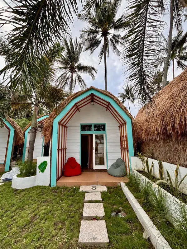 Petite maison de plage turquoise avec toit de chaume et chemin d'accès en pierre.