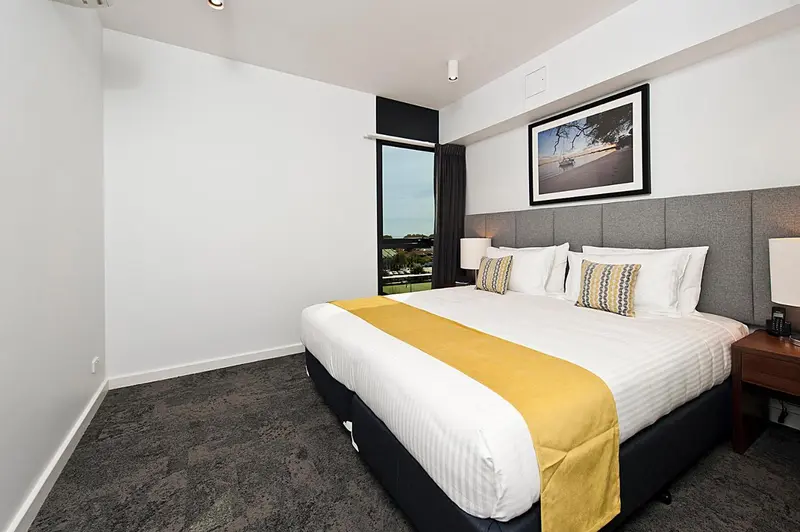 Une chambre lumineuse avec un grand lit recouvert d'une courtepointe jaune et de coussins.