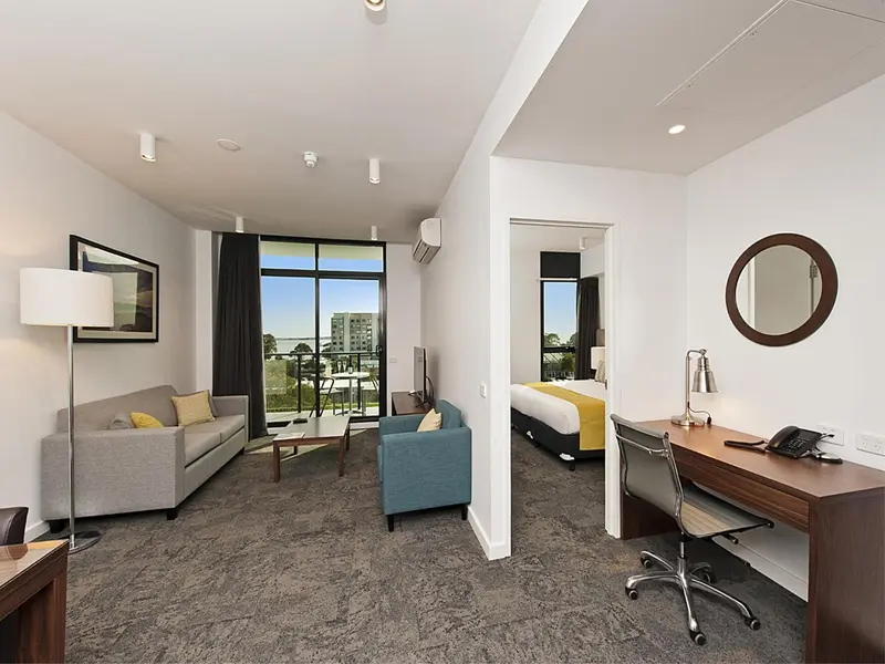 Espace de vie lumineux avec canapé, fauteuil et bureau donnant sur une vue urbaine.