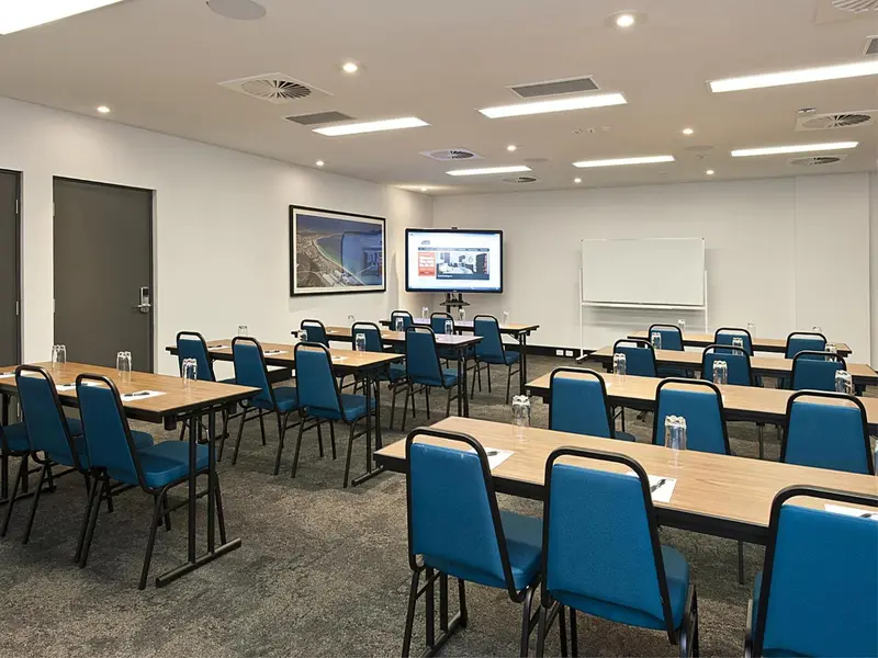Une salle de réunion lumineuse avec des tables et des chaises alignées face à un écran.