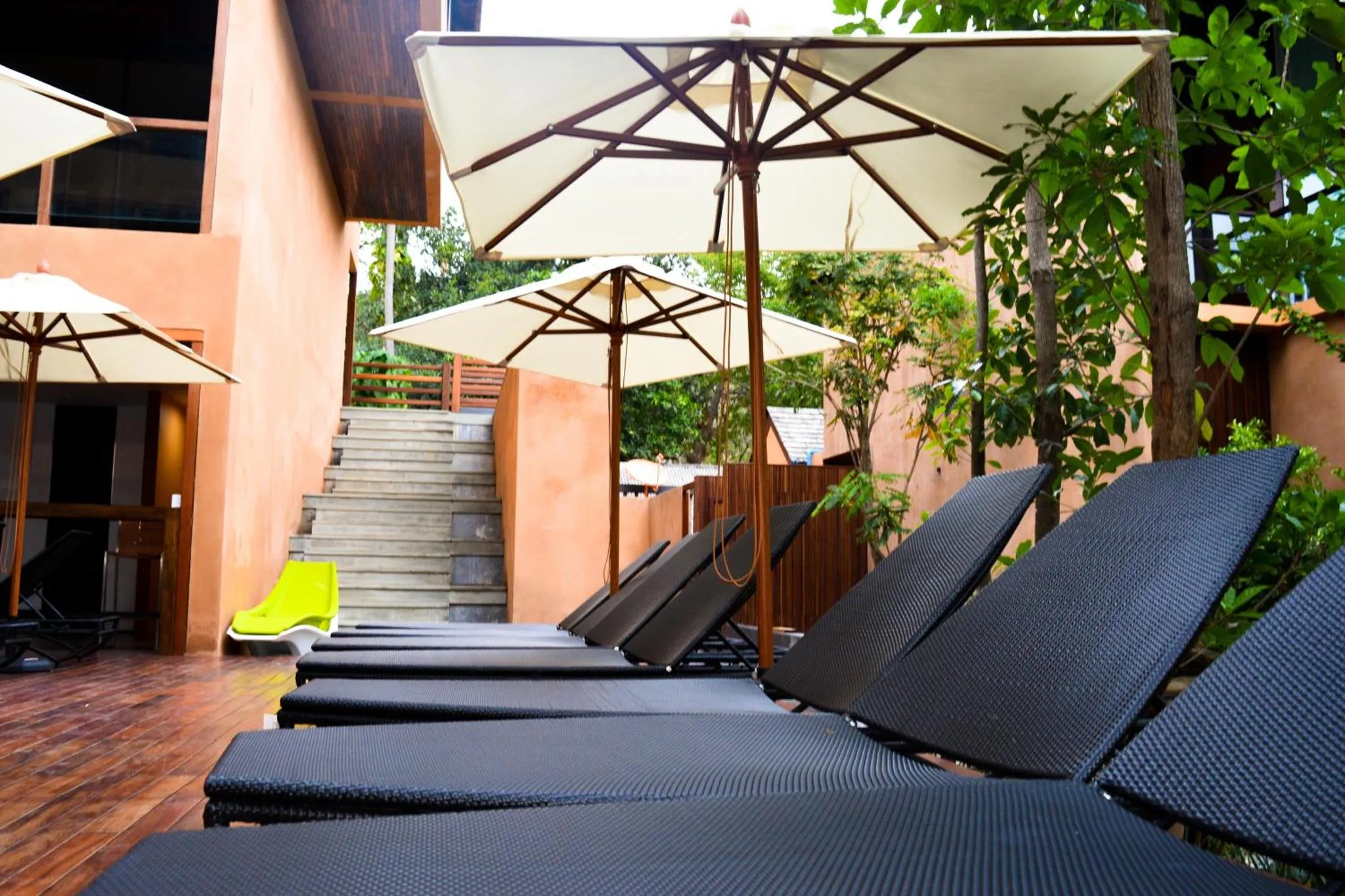 Transats noirs disposés sur une terrasse en bois ombragée par des parasols.