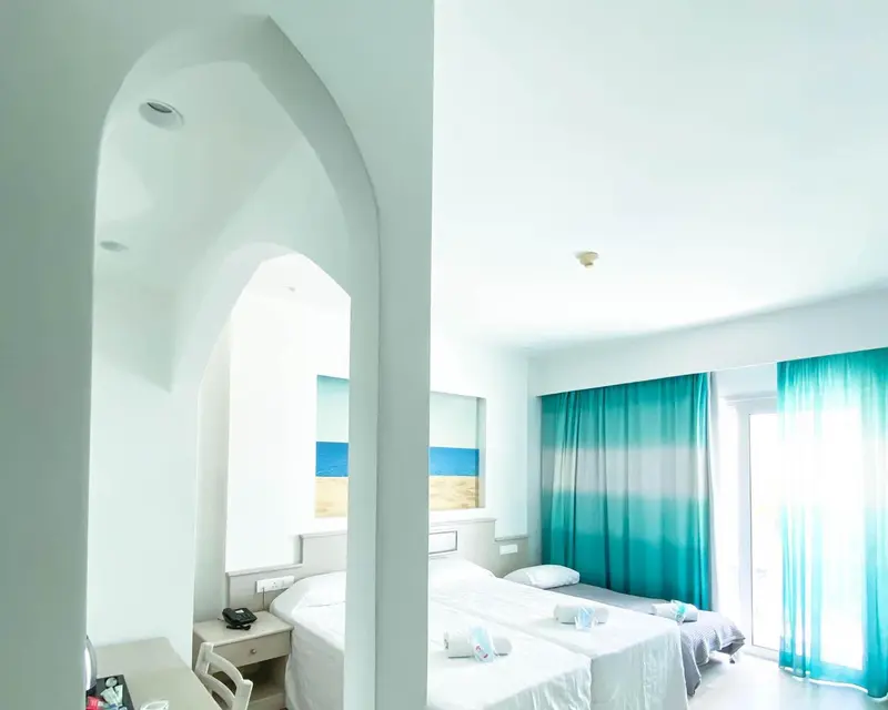 Chambre lumineuse avec deux lits simples et rideaux turquoise.