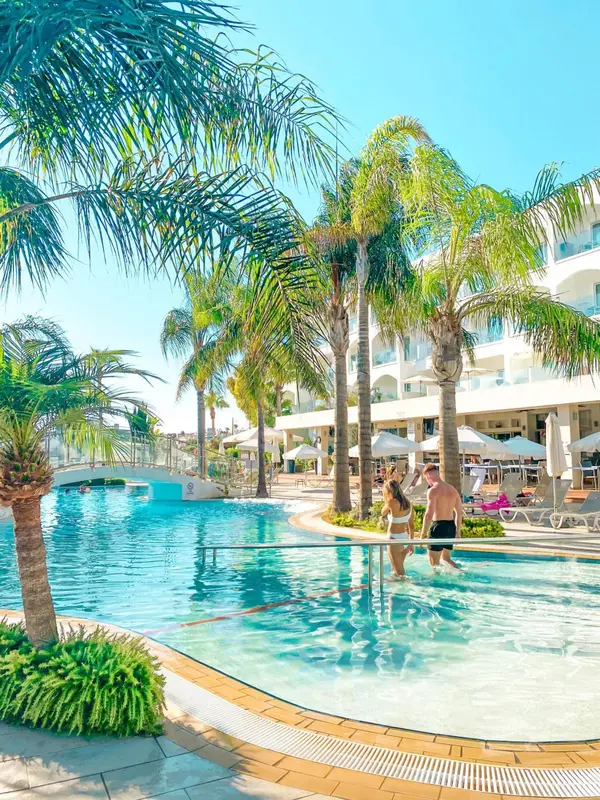 Une piscine turquoise bordée de palmiers et de transats blancs.