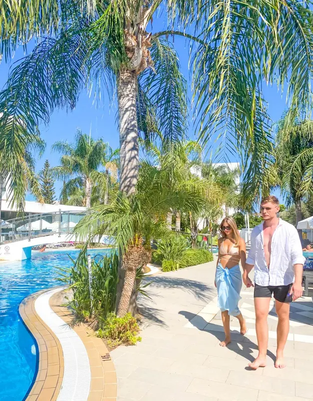 Un couple se promène le long d'une piscine bordée de palmiers.