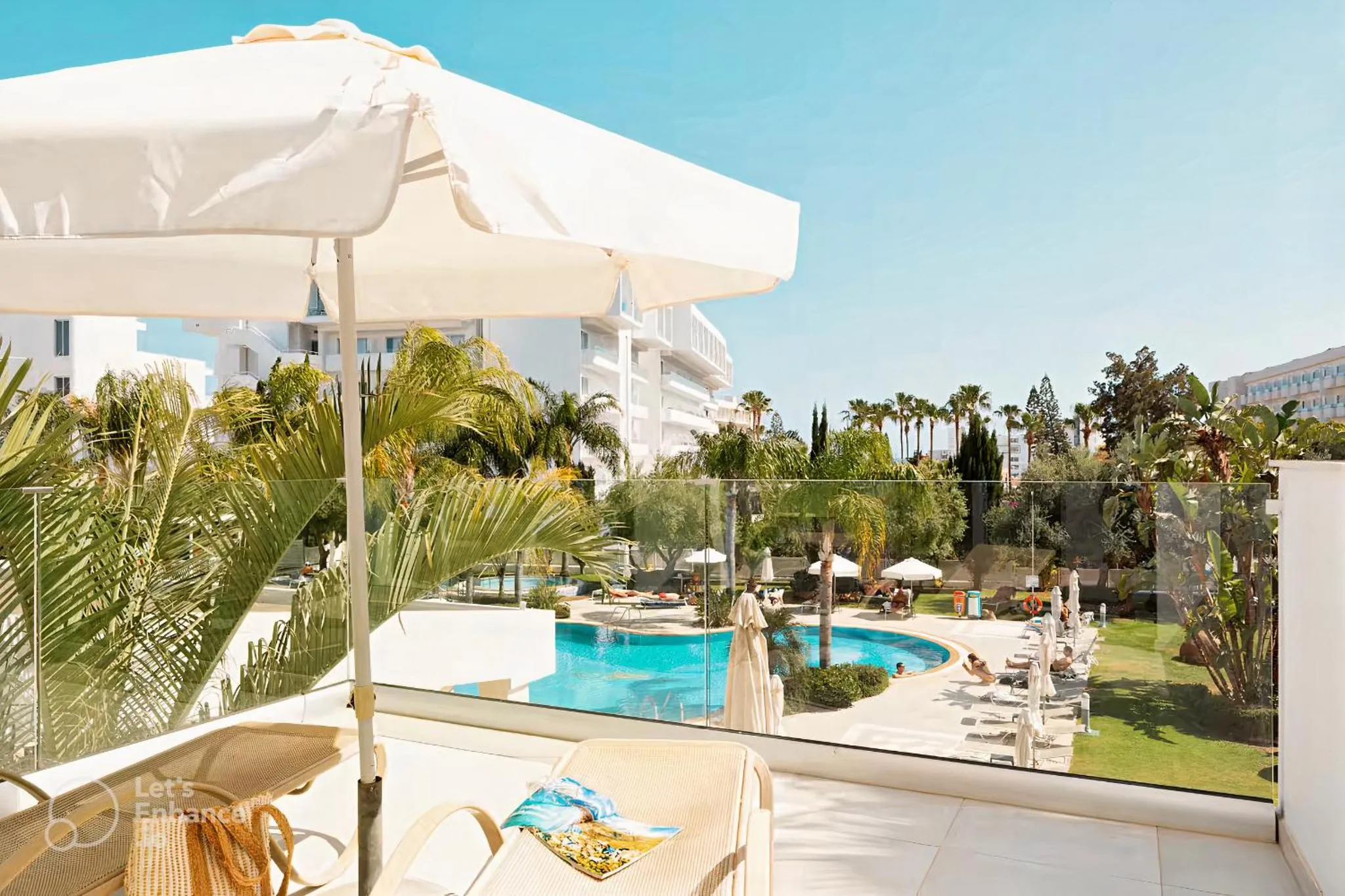Transats blancs disposés sur une terrasse ensoleillée avec vue sur une piscine et une végétation luxuriante.