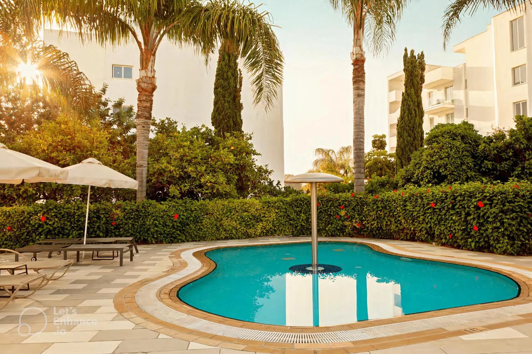 Une piscine rectangulaire avec un îlot central et des transats est entourée de végétation luxuriante et de palmiers.