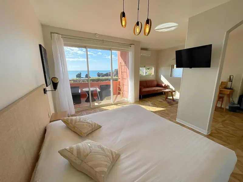 Une chambre lumineuse avec un grand lit donnant sur une terrasse et une vue sur la mer.