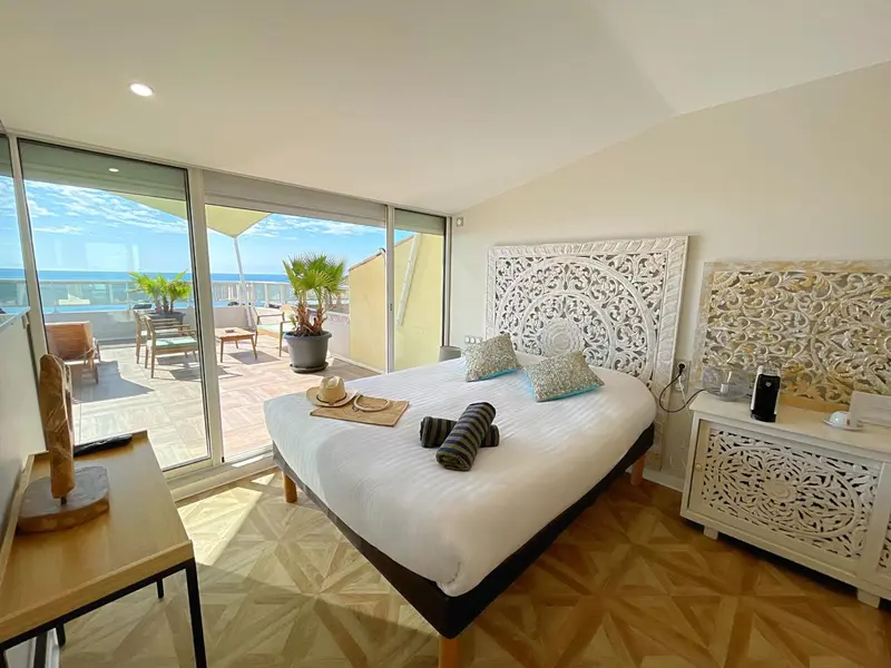 Une chambre lumineuse avec un grand lit donnant sur une terrasse ensoleillée.