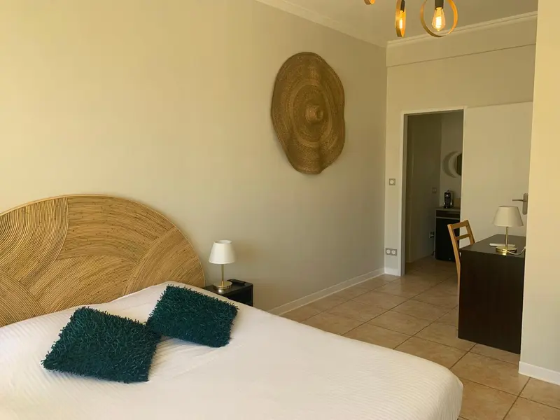 Une chambre lumineuse avec un lit recouvert d'une courtepointe blanche et de coussins verts.