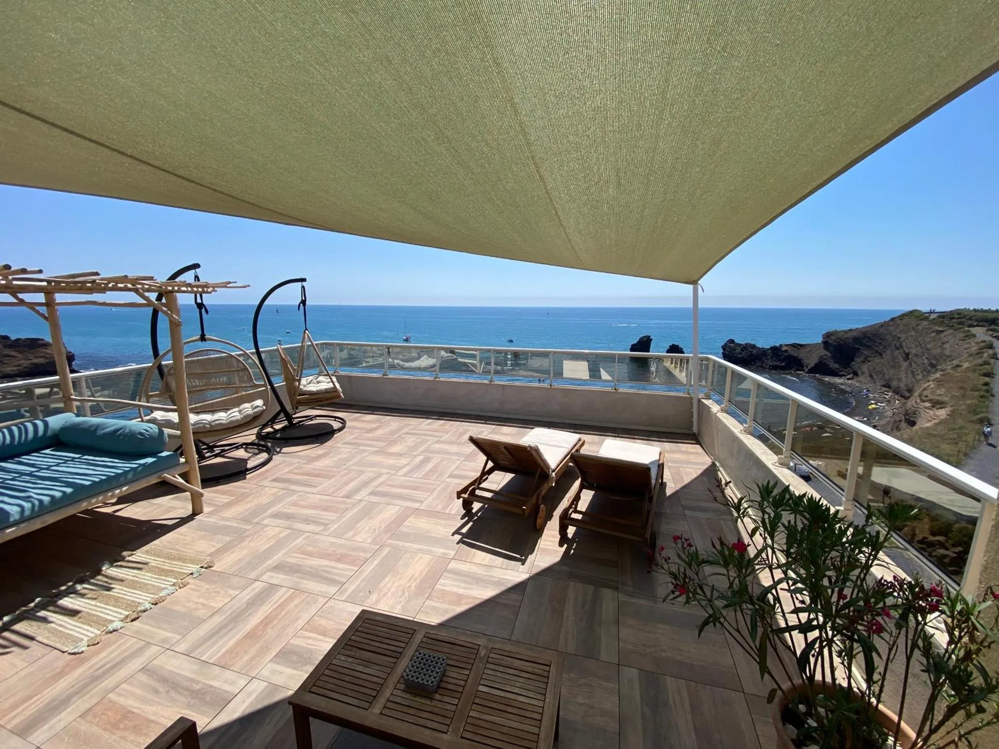Terrasse ombragée avec mobilier de détente et vue sur la mer.