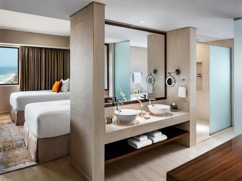 Chambre lumineuse avec deux lits et salle de bain attenante.