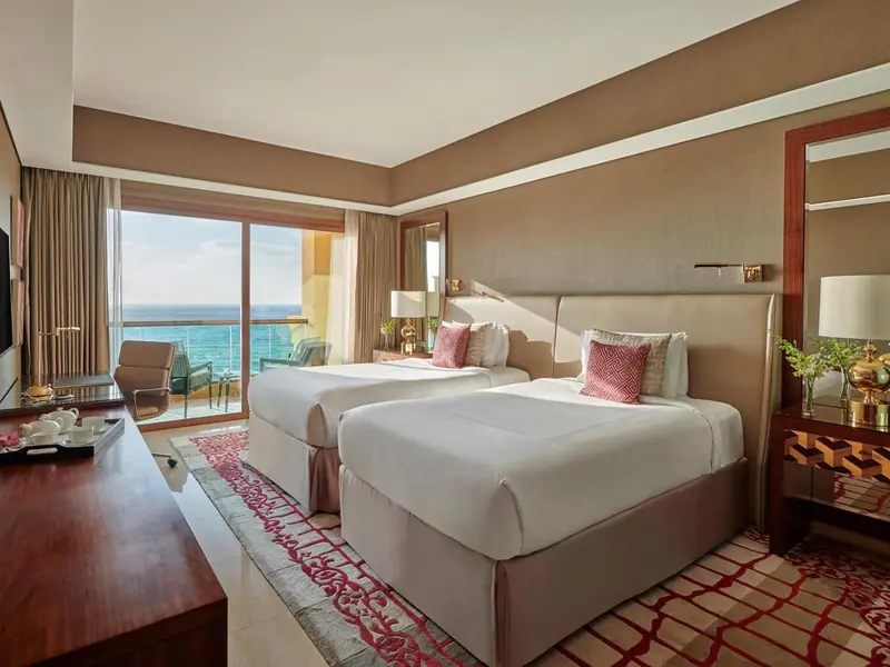 Chambre lumineuse avec deux lits et vue sur la mer.