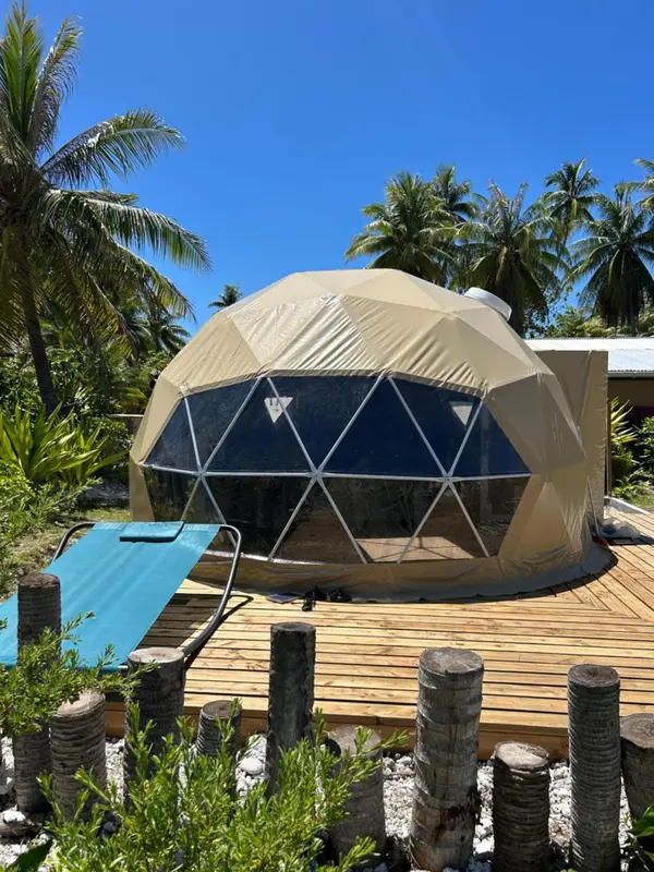 Une structure géodésique beige se dresse sur une terrasse en bois.
