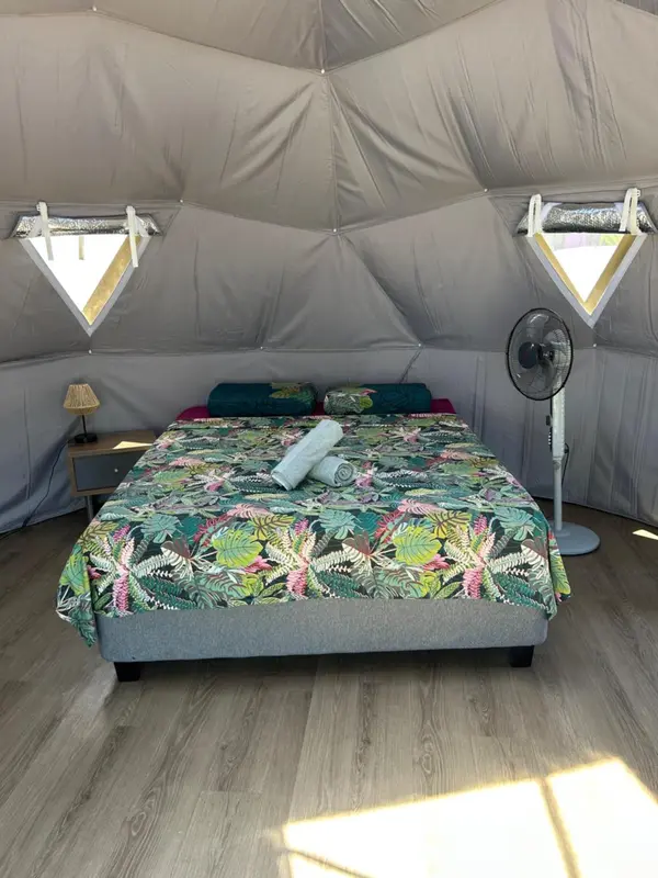 Une chambre avec un lit recouvert d'une couette à motifs tropicaux et un ventilateur.