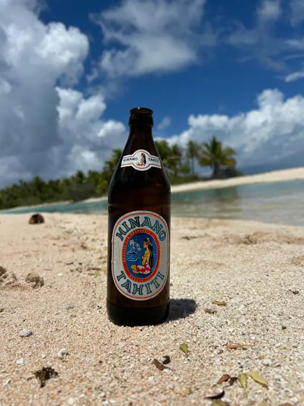 Une bouteille de bière sur une plage de sable blanc avec une eau turquoise en arrière-plan.