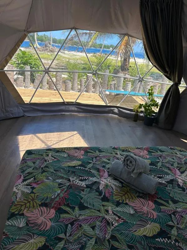 Intérieur d'une tente avec un lit et vue sur une plage.