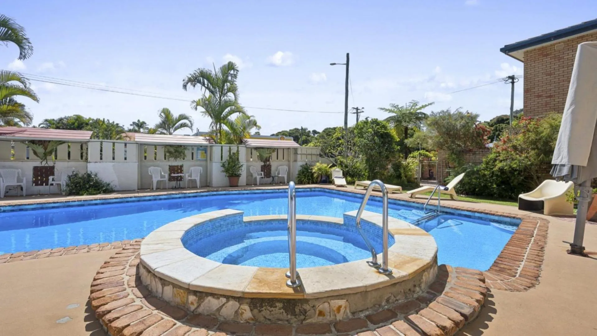 Piscine rectangulaire avec un jacuzzi intégré et des transats autour.