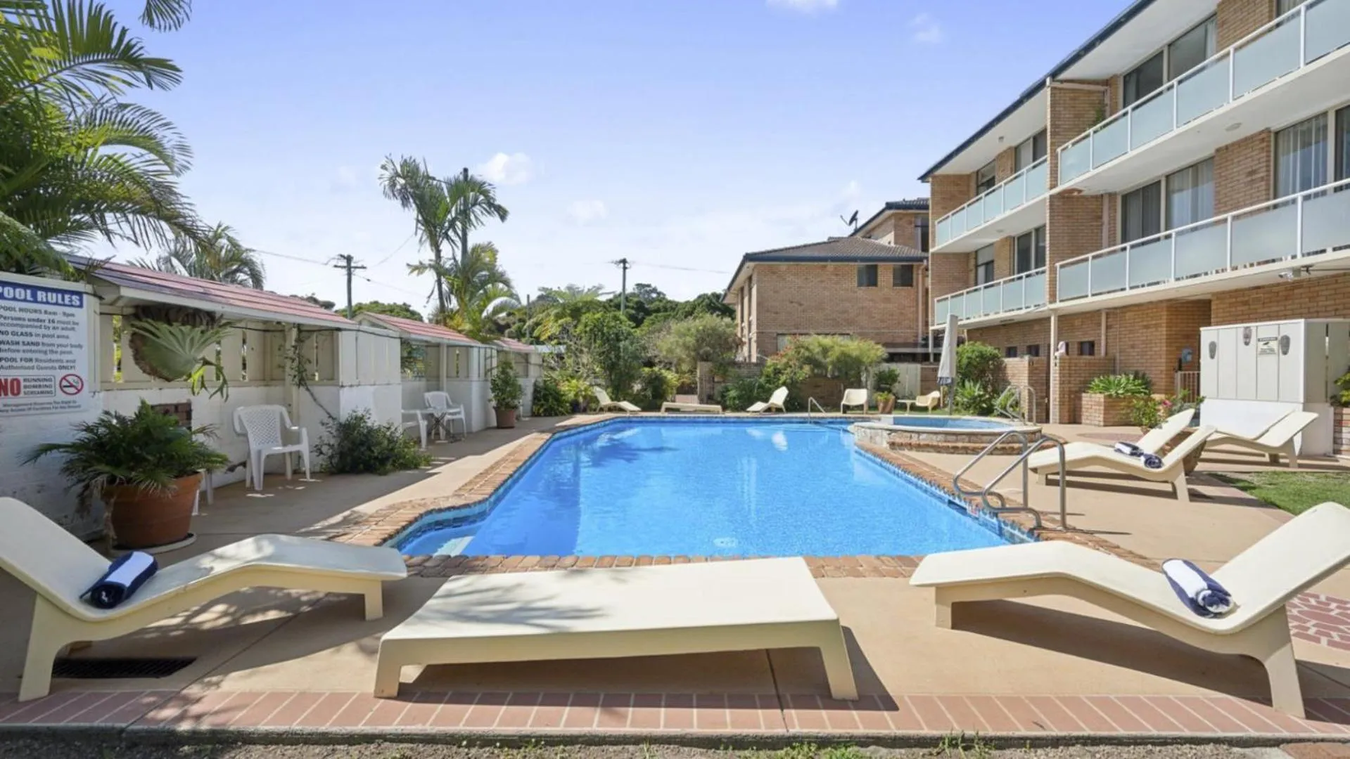 Transats blancs disposés autour d'une piscine rectangulaire turquoise dans un jardin tropical.