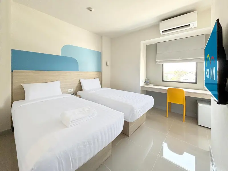 Chambre lumineuse avec deux lits simples et un bureau jaune.