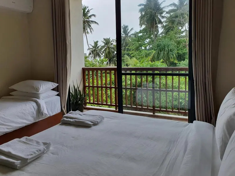 Une chambre lumineuse avec deux lits simples et une vue sur la végétation tropicale.