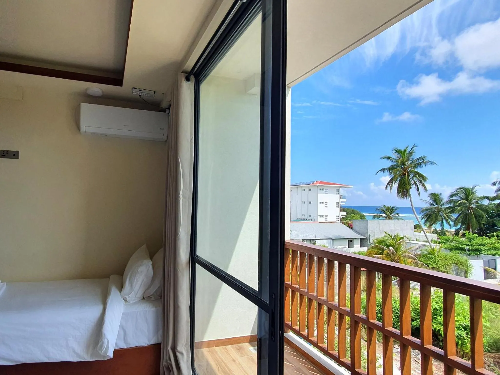 Une chambre lumineuse s'ouvre sur une terrasse avec vue sur la végétation et la mer.