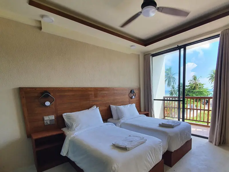 Une chambre lumineuse avec deux lits simples et vue sur la végétation.