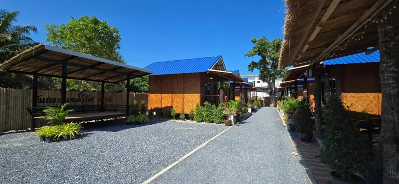 Petites maisons en bois avec toits en chaume et abris de jardin sur un sol gravillonné.