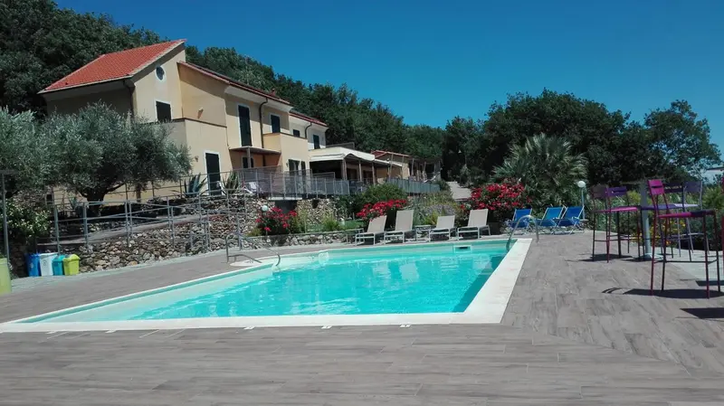 Une piscine rectangulaire bordée d'une terrasse ensoleillée devant un bâtiment jaune.
